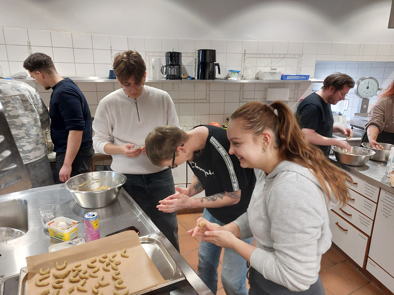 Drei junge Auszubildende stehen um einem Tisch mit einem Backblech und Schüsseln, unterhalten sich und kneten Plätzchenteig in der Küche der Gemeinde der Baptisten in Berlin-Schönberg beim 4. Azubitag der Auszubildenden von Werkstück Berlin mit Unterstützung von Immanuel Dienstleistungen Drei junge Auszubildende stehen um einem Tisch mit einem Backblech und Schüsseln, unterhalten sich und kneten Plätzchenteig in der Küche der Gemeinde der Baptisten in Berlin-Schönberg beim 4. Azubitag der Auszubildenden von Werkstück Berlin mit Unterstützung von Immanuel Dienstleistungen