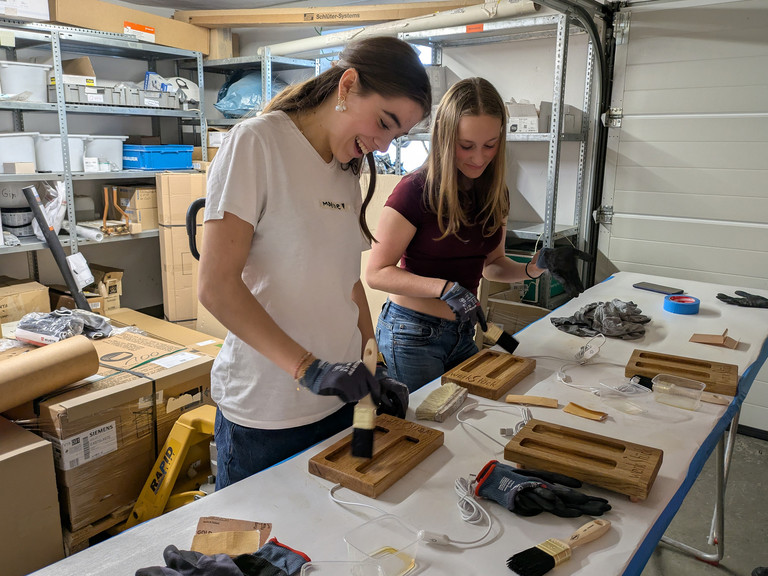 Mädchen haben Spaß beim Auftragen von Holzöl auf Handyhalter - Werkstück Raumgestaltung & Versorgungstechnik
