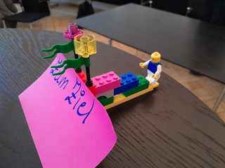 Ein Segelboot aus bunten Legosteinen mit einem lila Papierstück mit der Aufschrift "Zum Ziel" auf dem Tisch beim Teamtag vom Meisterbetrieb für Handwerk Werkstück Berlin zum Thema "Gute Kommunikation verbindet" in Berlin-Wannsee